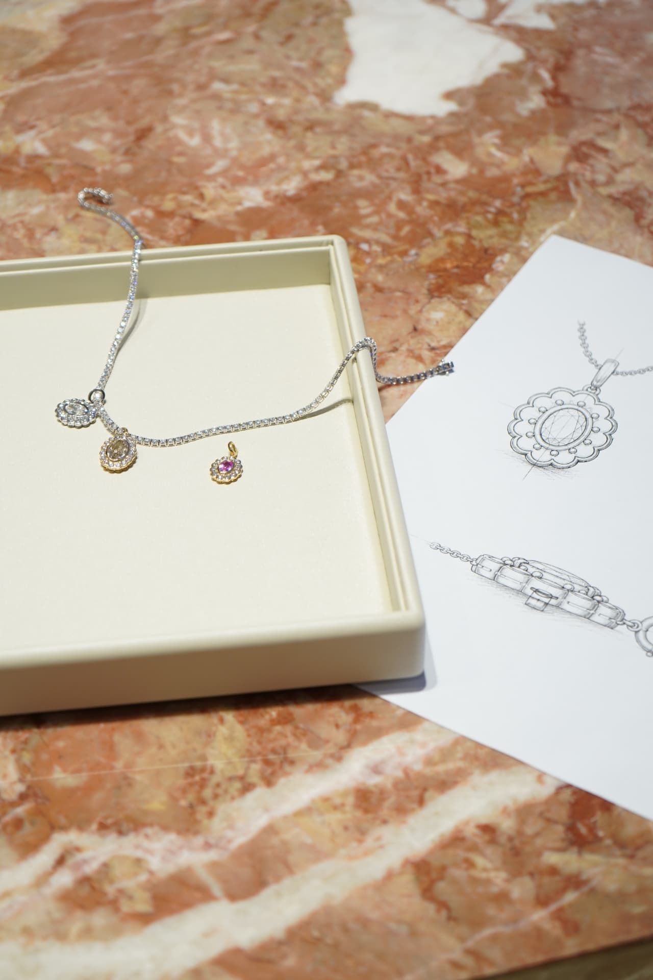 A diamond necklace on an ivory presentation tray beside its original design sketch